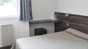 A hotel room with a bed, a small desk, a window with curtains, and a wall-mounted air conditioner. - Henri 4 (Rostrenen)