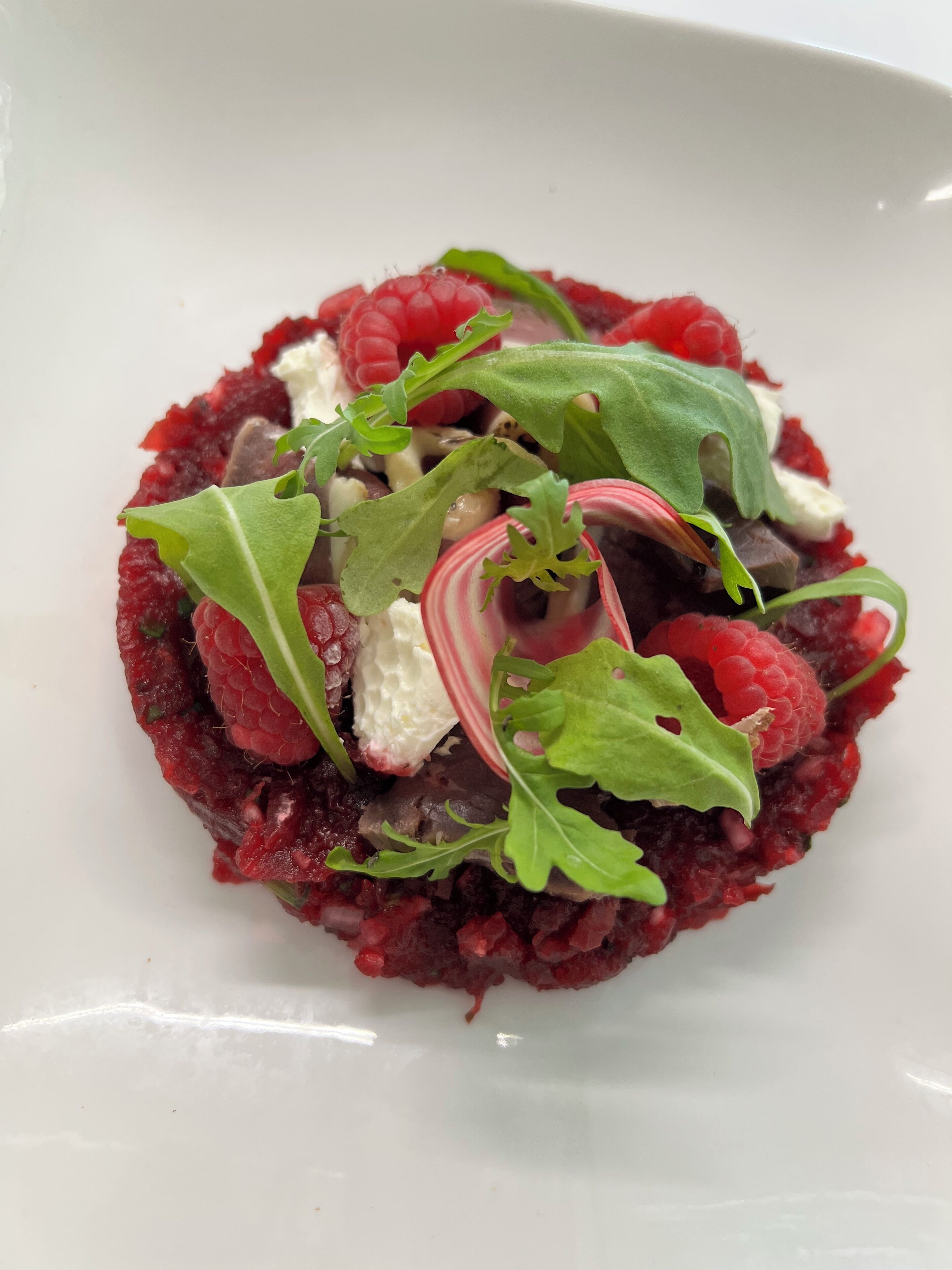A dish with raspberries, arugula, and a creamy topping on a white plate.