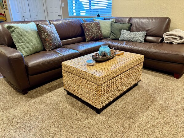A brown leather sectional sofa with multiple cushions, a woven coffee table with decorative items, and a beige carpet. - 1BD Ski-in/Ski-out Condo Near Lift 8 & 1. Grab a Lift and Ski To Either Lodge. (Brian Head)