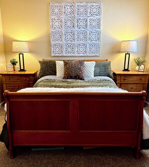 A bed with a wooden frame, two bedside tables with lamps, and a decorative wall piece above. - 1BD Ski-in/Ski-out Condo Near Lift 8 & 1. Grab a Lift and Ski To Either Lodge. (Brian Head)