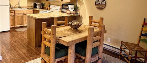 Cuina amb armaris de fusta, una illa central i una zona de dinar amb taula i cadires de fusta.