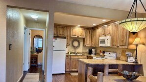 Una cocina con armarios de madera, un refrigerador, un microondas y un comedor con mesa y sillas.