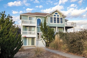 A two-story house with a balcony on the upper floor, a front entrance with steps, and a small porch.