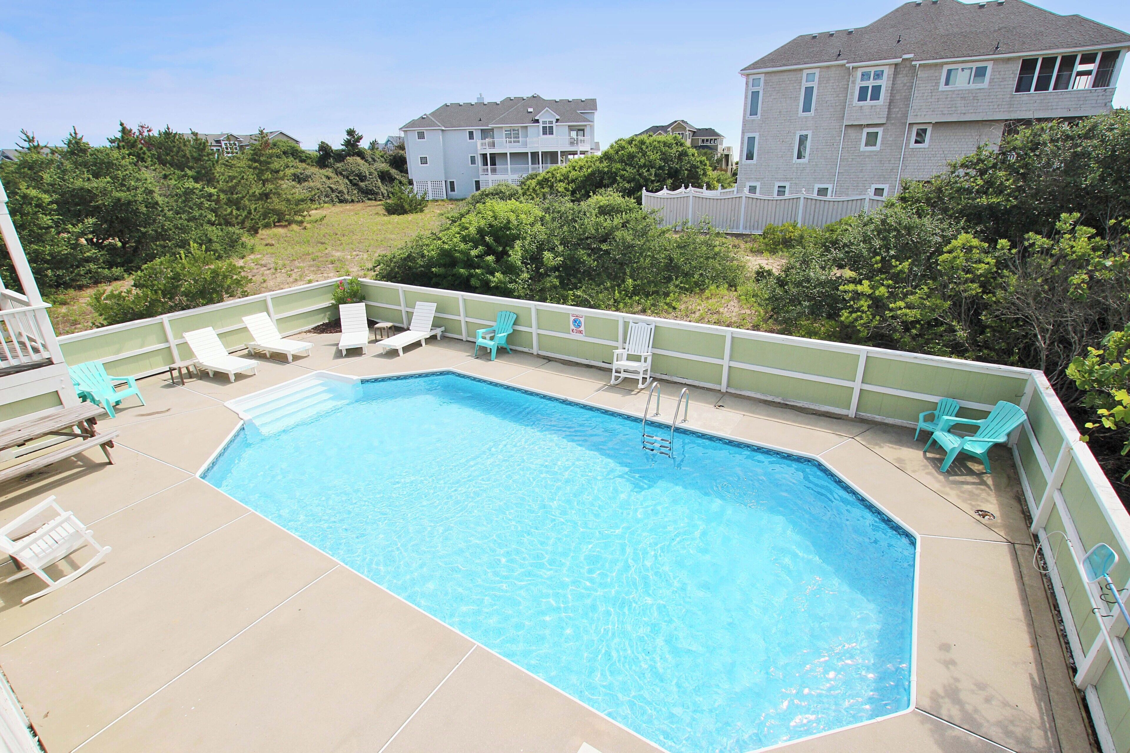 A rectangular swimming pool with a white deck, surrounded by white and turquoise lounge chairs.