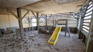 A sandy indoor play area with a yellow slide, wooden beams, and a fenced enclosure. - Oceanside, 400 ft to Beach access, screened porch, SNH416, Ocean Adventure (Nags Head)