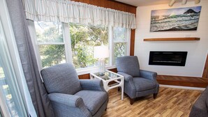 A living room with two grey armchairs, a small white coffee table, a lamp, a flat-screen TV mounted on the wall, and a window with curtains. - Oceanside, 400 ft to Beach access, screened porch, SNH416, Ocean Adventure (Nags Head)