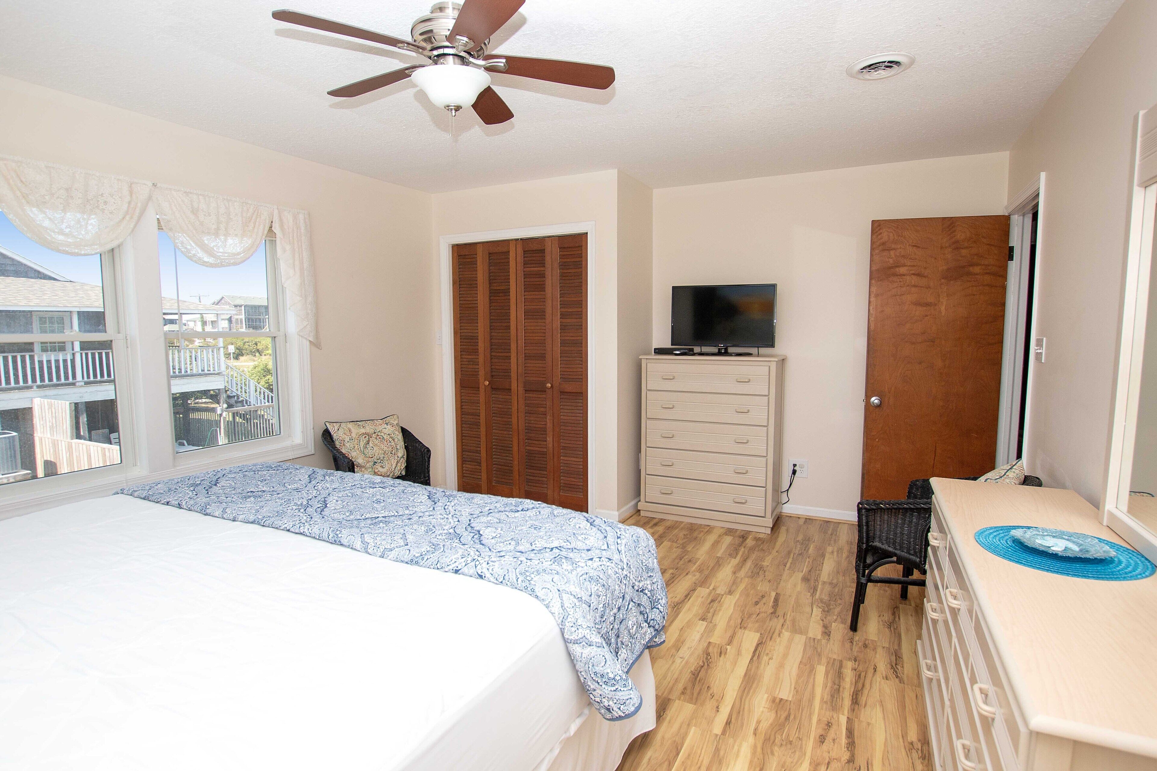 A bedroom with a bed, a dresser, a television, and a ceiling fan.