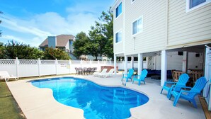 A backyard with a swimming pool, lounge chairs, and a patio area.
