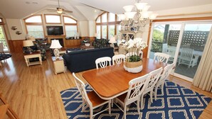 Un vaste espace de vie comprenant une table à manger en bois, des chaises blanches et un tapis à motifs bleus.