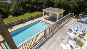 Une piscine dotée d’une terrasse en bois et de chaises longues, entourée d’une clôture en bois et d’arbres.