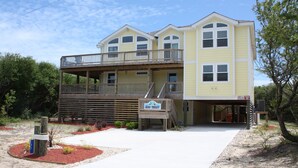 Une maison à deux étages avec un balcon, une enseigne indiquant « Thérapie de groupe », et une allée menant à la maison recouverte de sable.
