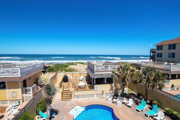 A beachfront hotel with a pool, lounge chairs, and a view of the ocean.