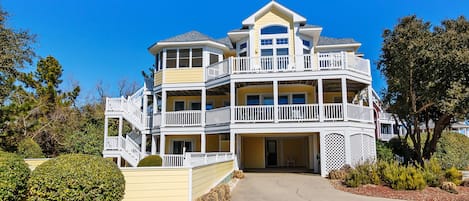 A multi-story house with a balcony, a driveway, and a well-maintained garden.