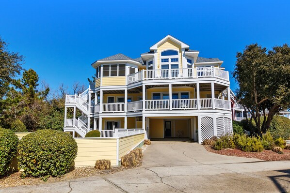 A multi-story house with a balcony, a driveway, and a well-maintained garden.
