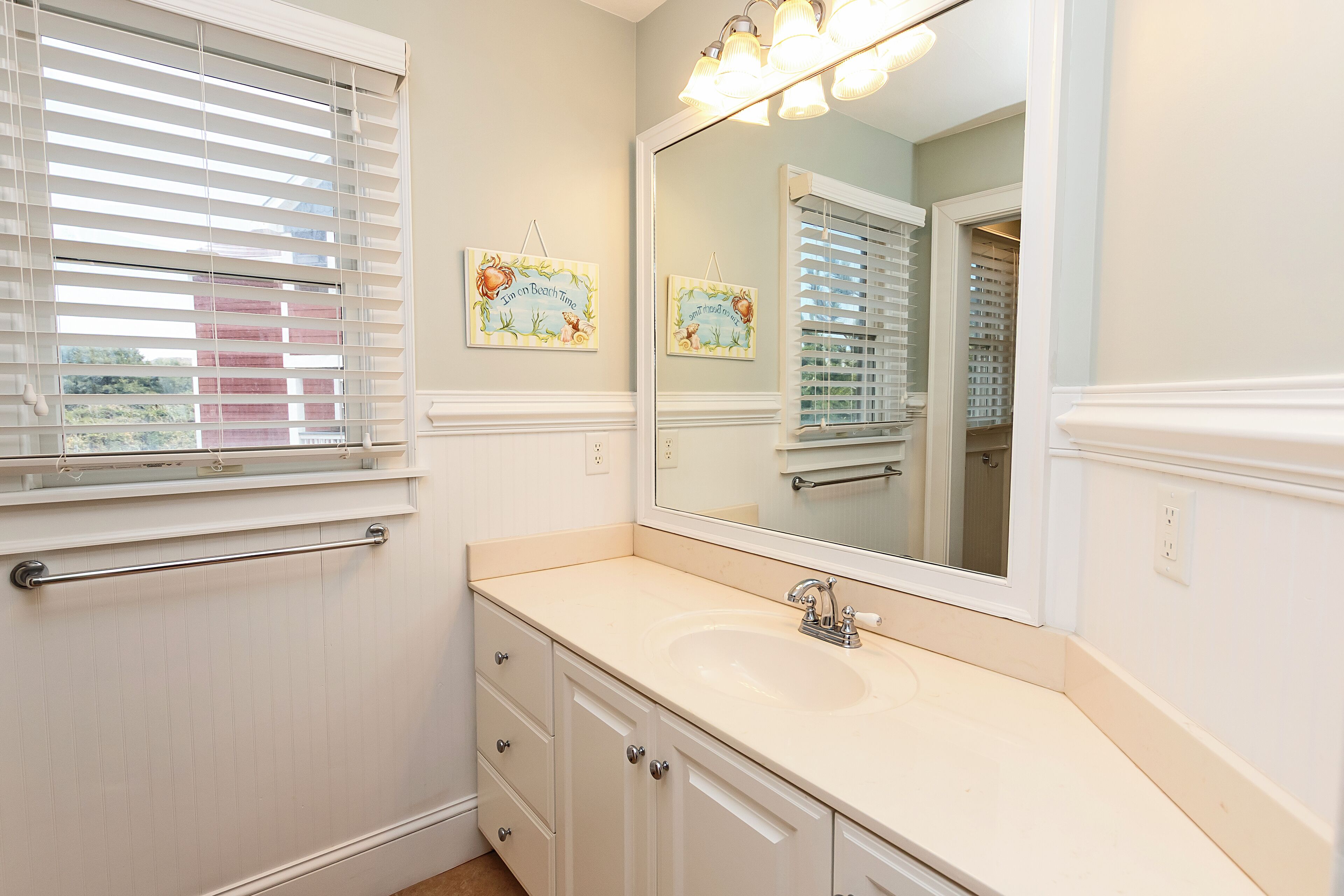 A bathroom with a large mirror, a sink, and a window with blinds.