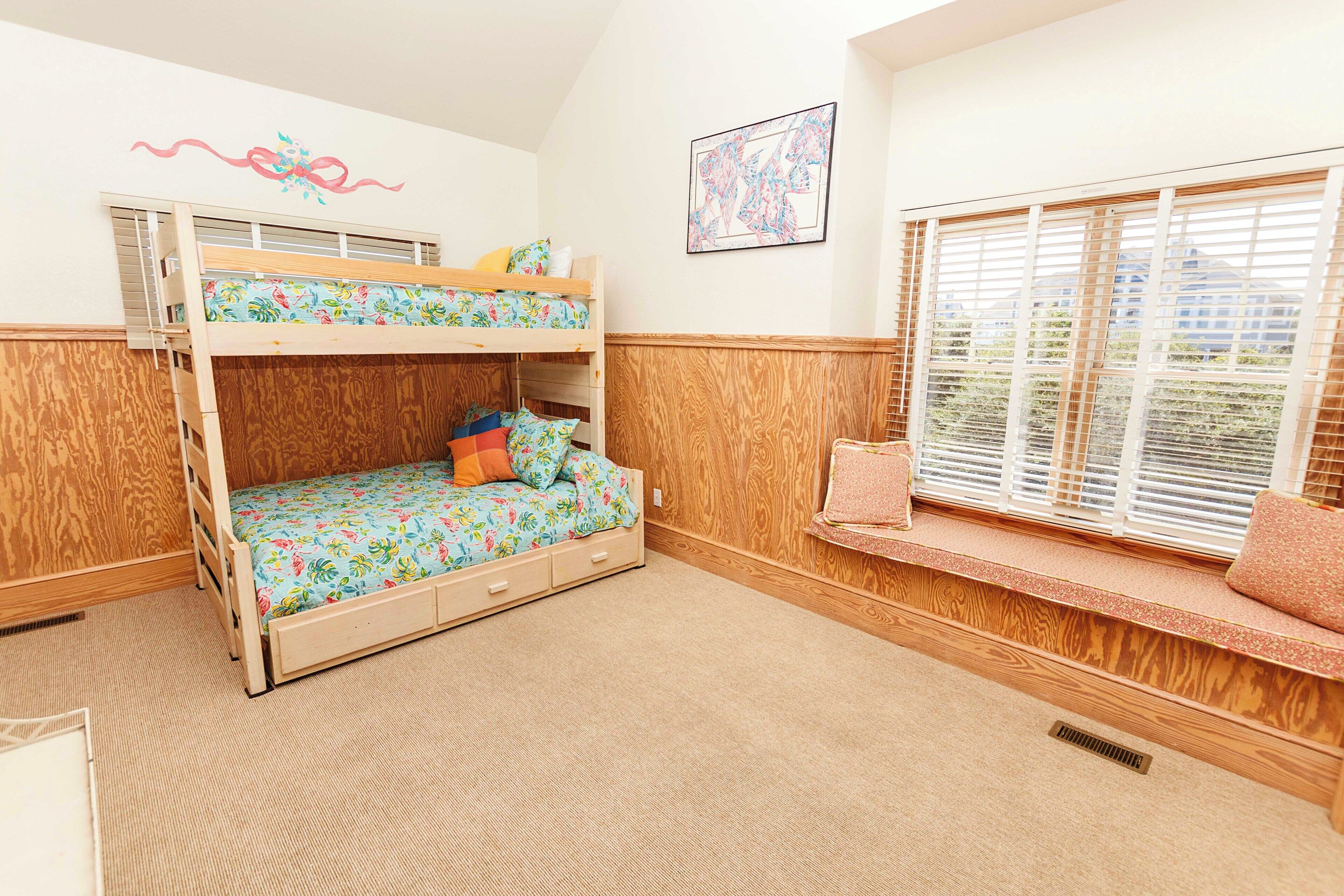 A bunk bed with a floral bedspread, a window seat with a cushion, and a wall-mounted shelf.