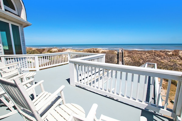 A deck with white railings and chairs overlooking a beach.