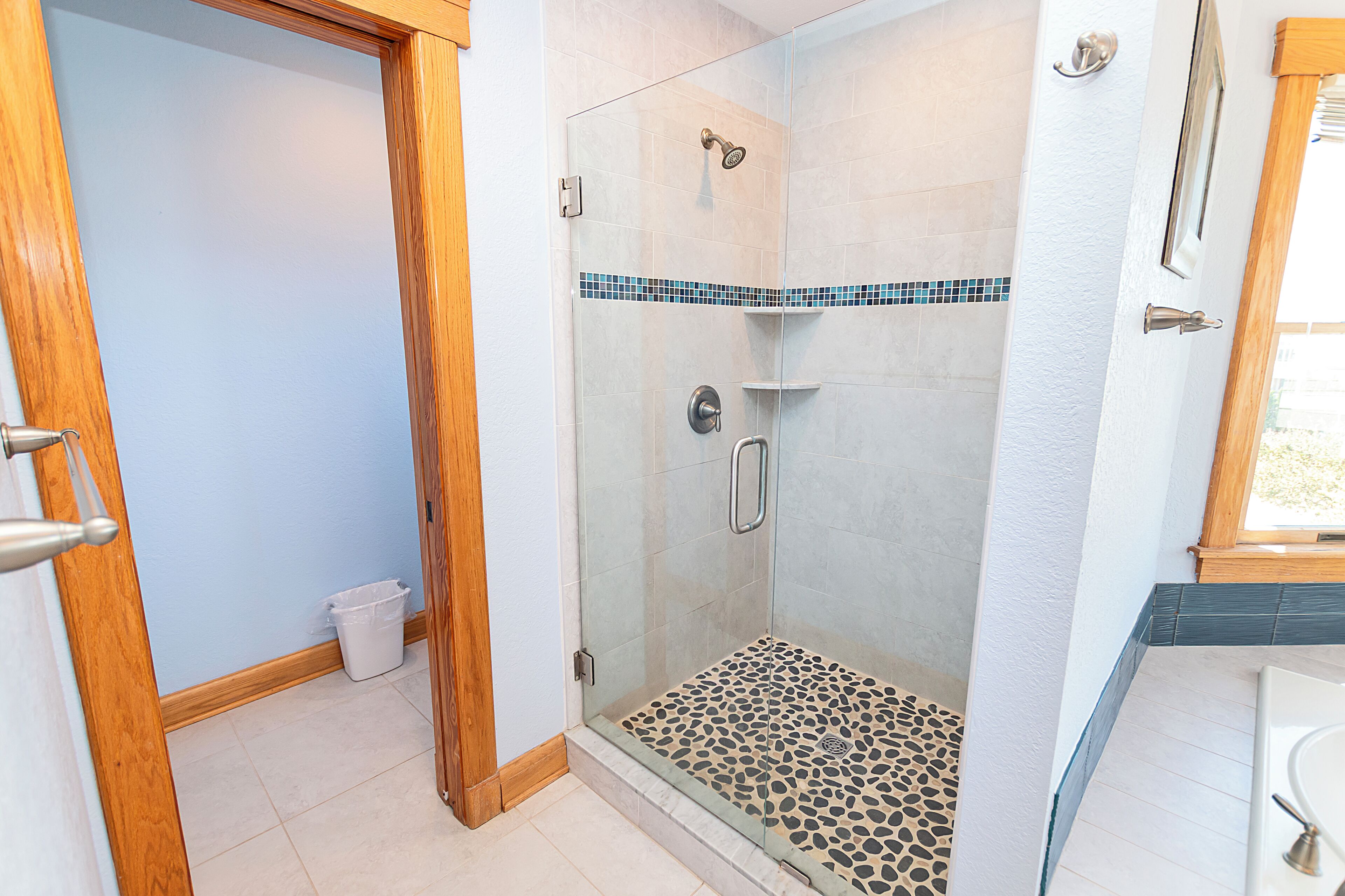 A glass-enclosed shower with a tiled floor, a showerhead, and a handrail.
