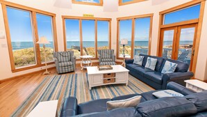 A spacious living room with large windows, a blue sofa, striped armchairs, and a white coffee table. - OCEANFRONT, 9 BRs, Private Pool, Theater Rm, Rec Rm, Ocean Views, PI134, Heavenly Dayz (Corolla)