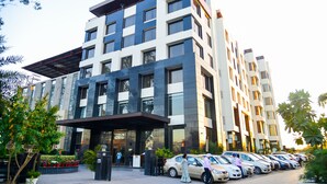 A multi-story hotel with a modern design, featuring a covered entrance and a parking area with several cars. - Hotel Almeida (Dera Bassi)