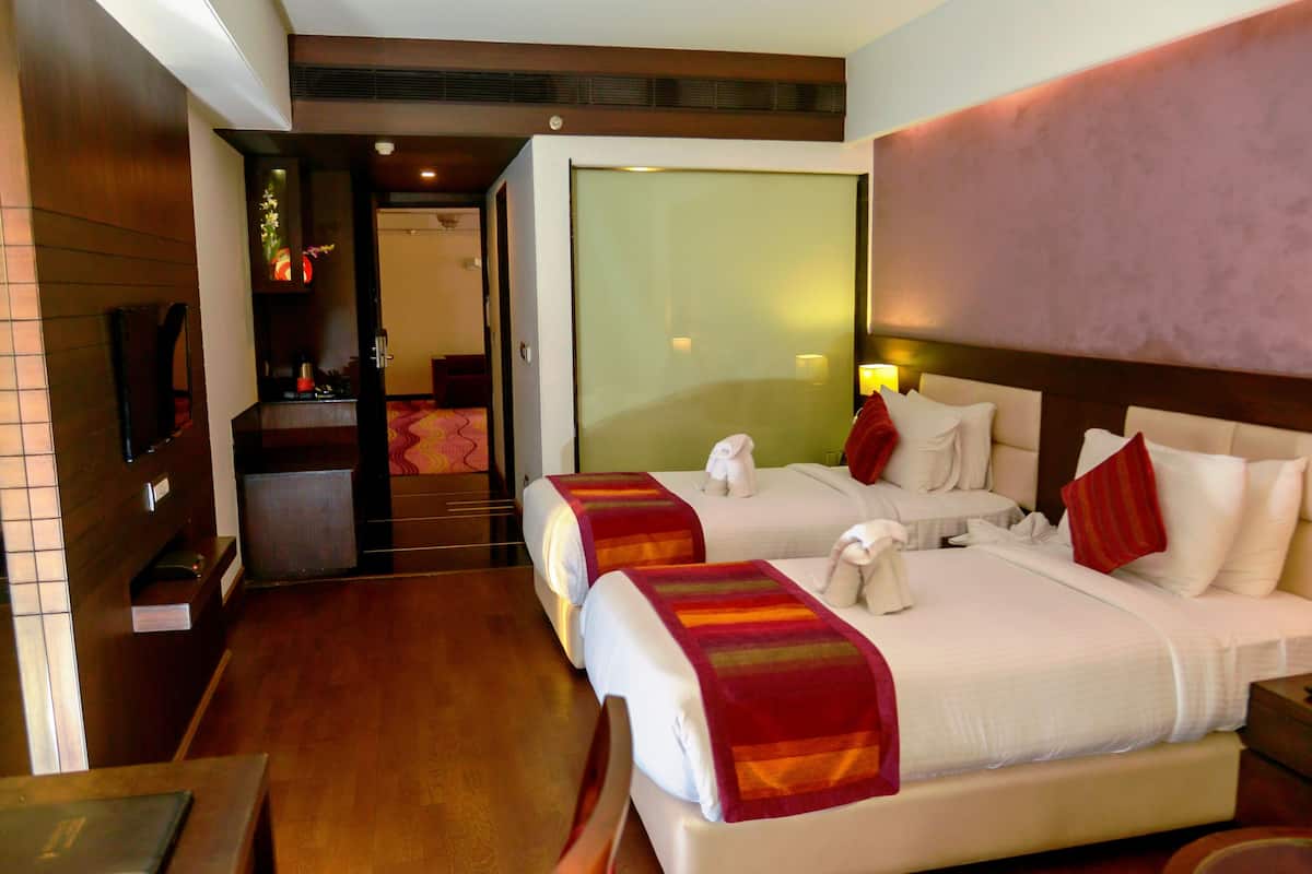 A hotel room with two beds, a wooden floor, a TV, and a bathroom visible through an open door.