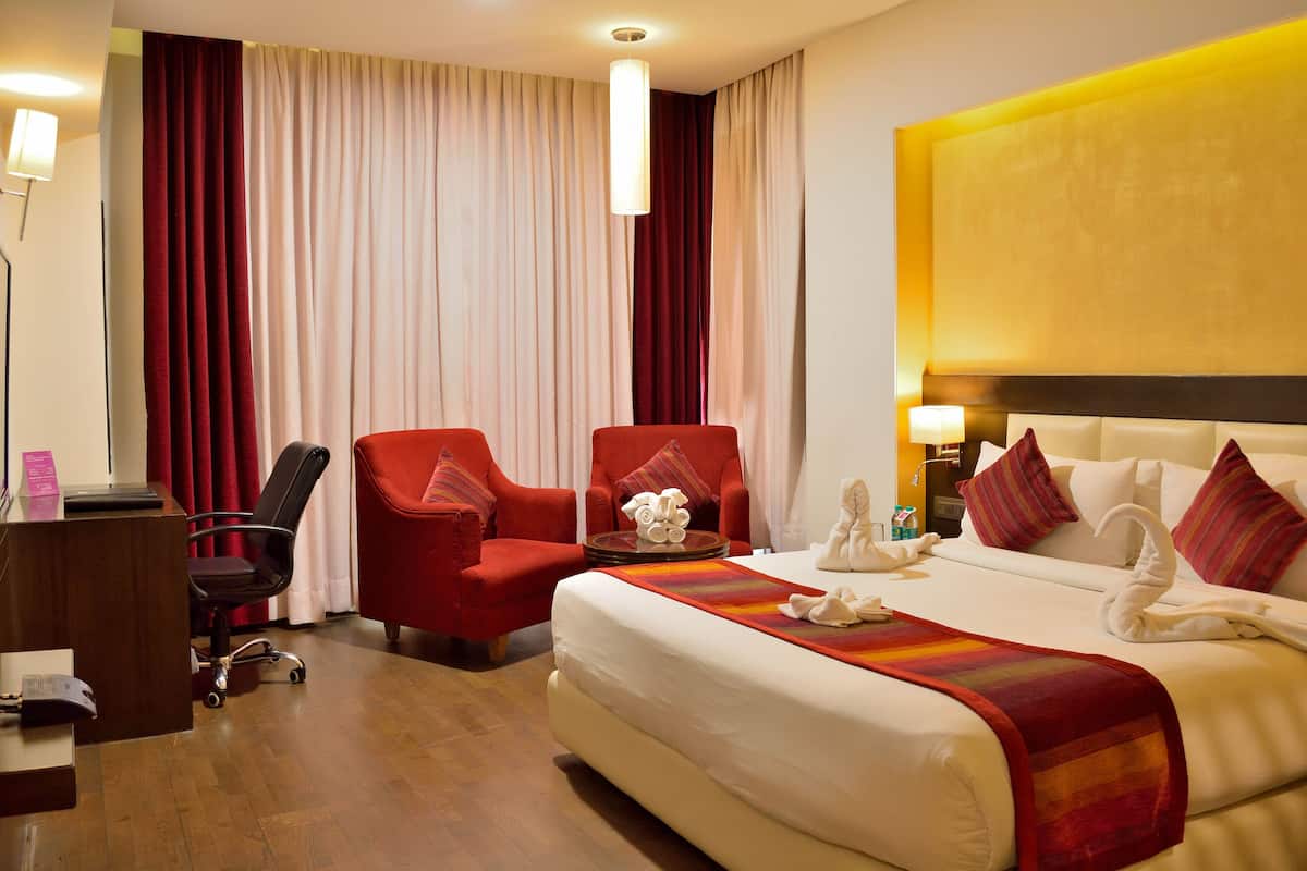 A hotel room with a large bed, two red armchairs, a desk with a computer, and a view of the curtains.
