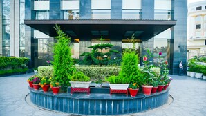 A circular planter with various potted plants and flowers in front of a modern building. - Hotel Almeida (Dera Bassi)
