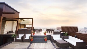 A rooftop terrace with outdoor seating, a bar area, and a view of the cityscape. - Hotel Almeida (Dera Bassi)