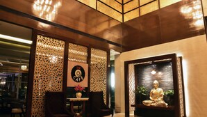 A lobby with a Buddha statue, a sign reading "The Cafe," and two chairs with a small table and vase. - Hotel Almeida (Dera Bassi)
