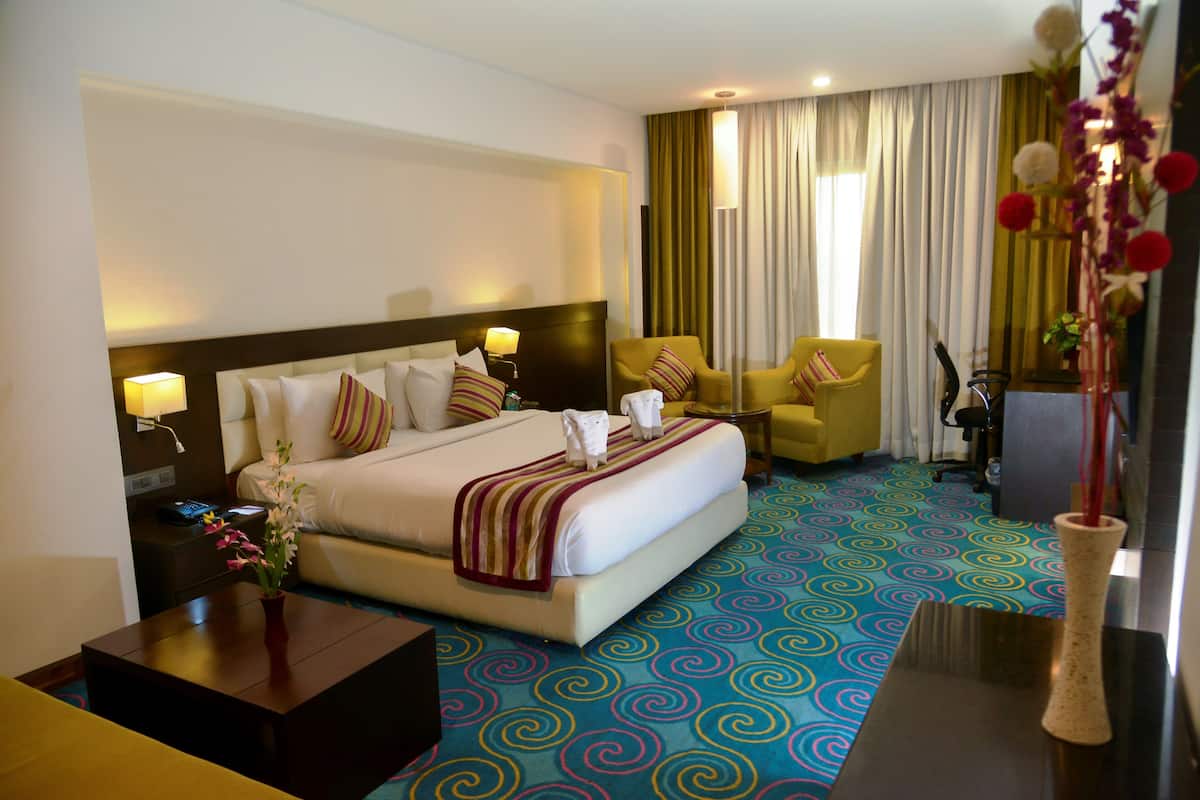 A hotel room with a large bed, two chairs, a desk, and a vase with flowers.