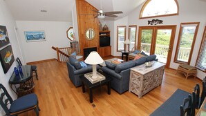 A spacious living room with a fireplace, a ceiling fan, and a balcony with wooden railings. - Oceanside, Hot Tub, Screened porch, Close to Beach, OS9H, Starfisher (Corolla)