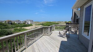 A wooden deck with a railing, overlooking a beach and houses. - Oceanside, Hot Tub, Screened porch, Close to Beach, OS9H, Starfisher (Corolla)