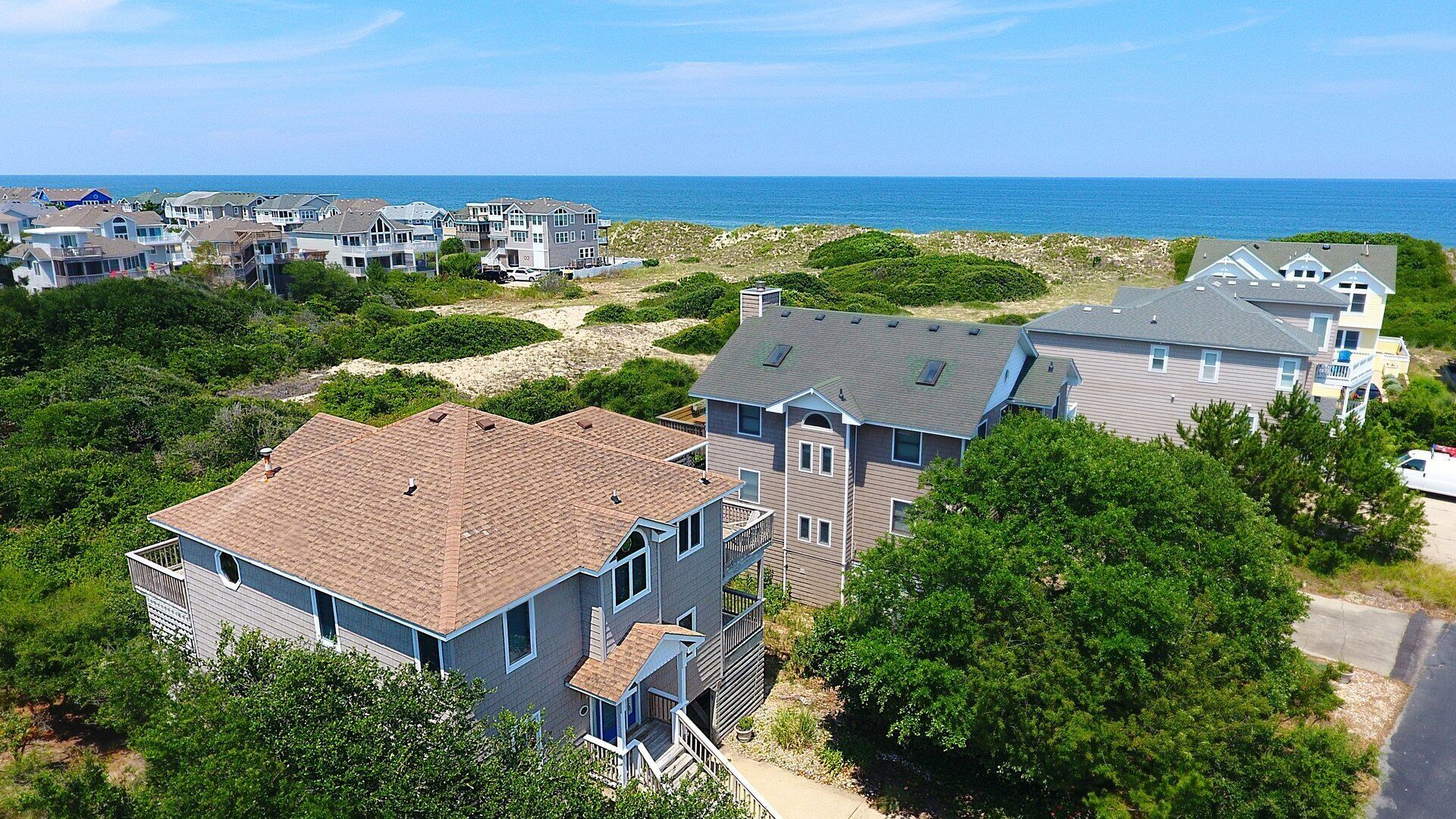 A coastal residential area with houses featuring multiple stories, some with balconies, and a view of the ocean.