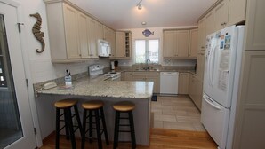 A kitchen with a central island, bar stools, a refrigerator, and a fish decoration on the wall. - Oceanside, Hot Tub, Screened porch, Close to Beach, OS9H, Starfisher (Corolla)