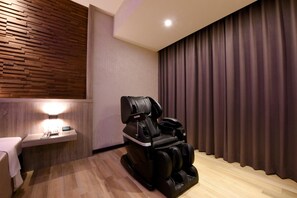 A massage chair in a room with wooden paneling, a small table with a phone, and a curtain. - Purple Rainbow Motel (New Taipei City)