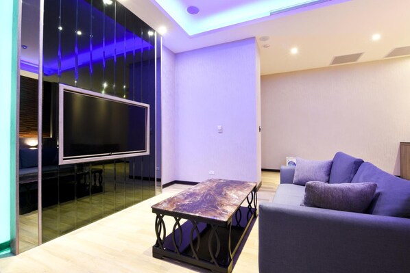 A modern living room with a flat-screen TV mounted on a glass wall, a wooden coffee table, and a purple sofa. - Purple Rainbow Motel (New Taipei City)