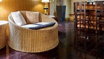 A wicker sofa with cushions, a table lamp, a vase with branches, and a dining area with chairs.