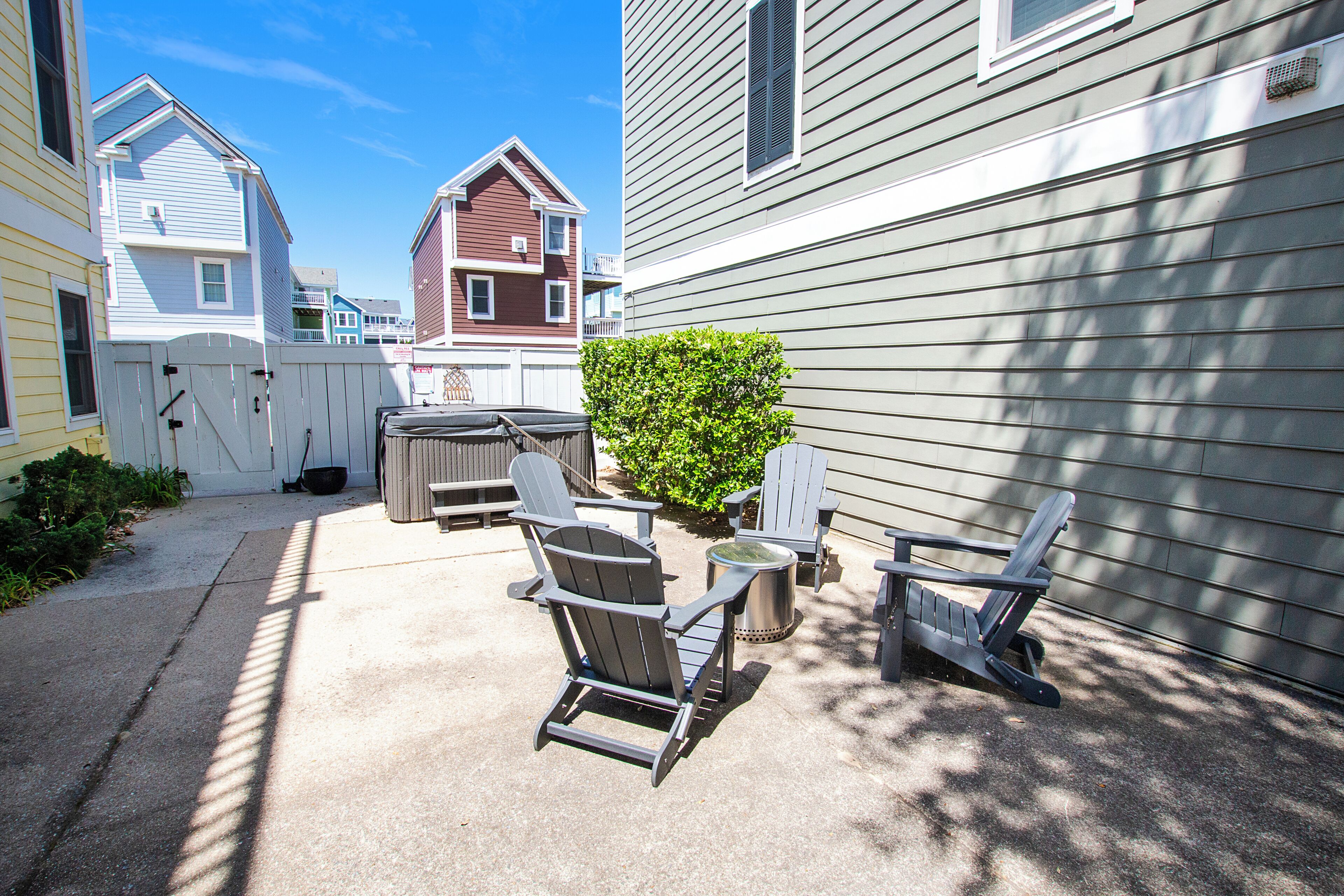 A patio with Adirondack chairs, a fire pit, and a small bush.