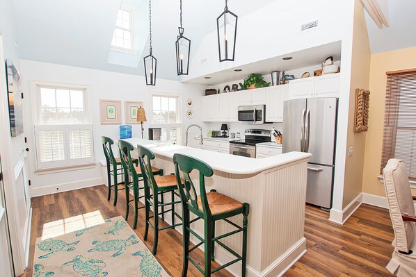 A modern kitchen with white cabinetry, a stainless steel refrigerator, and a bar area with green chairs.