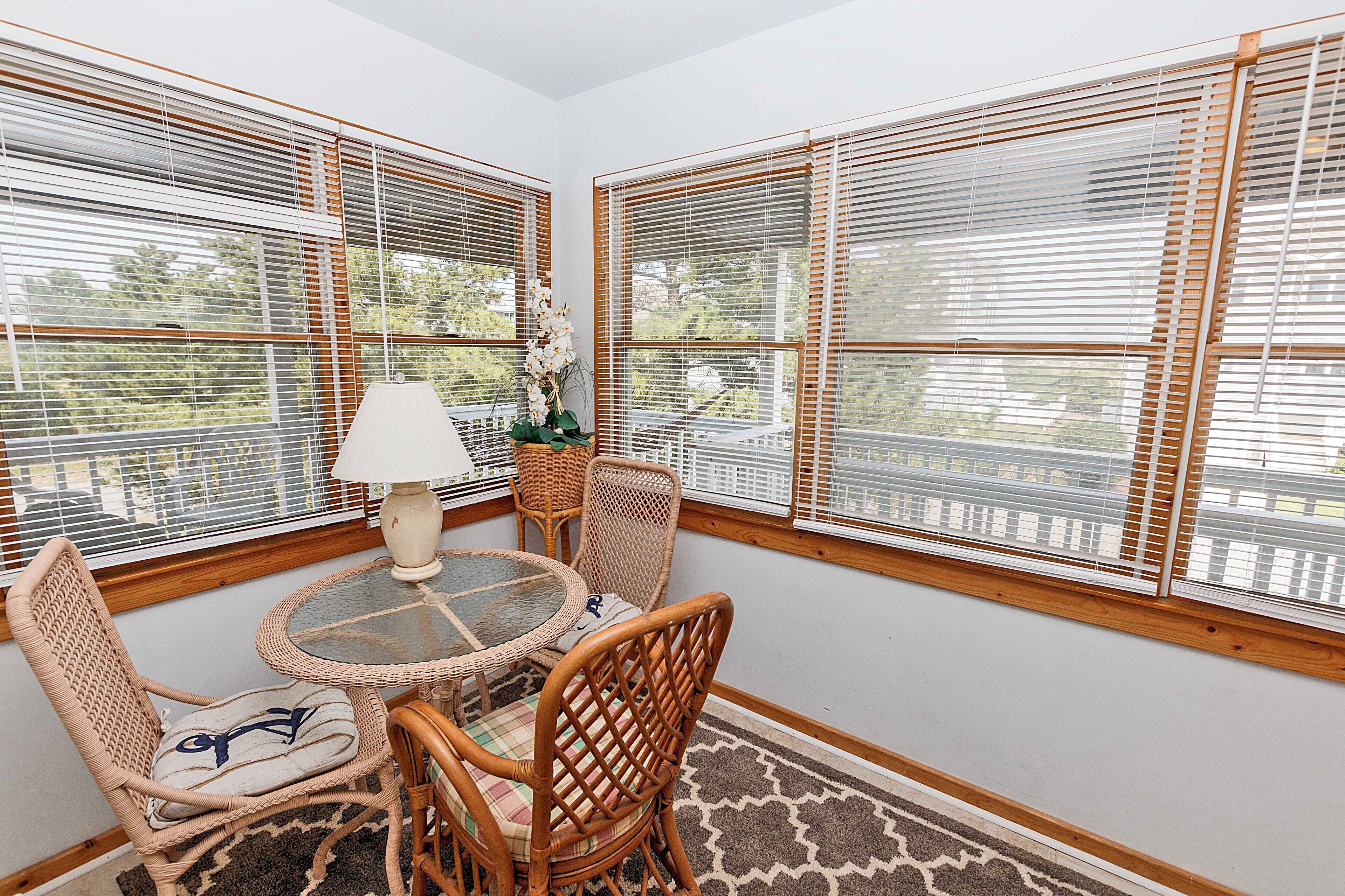 A corner room with a round glass table, wicker chairs, a lamp, and a potted plant.
