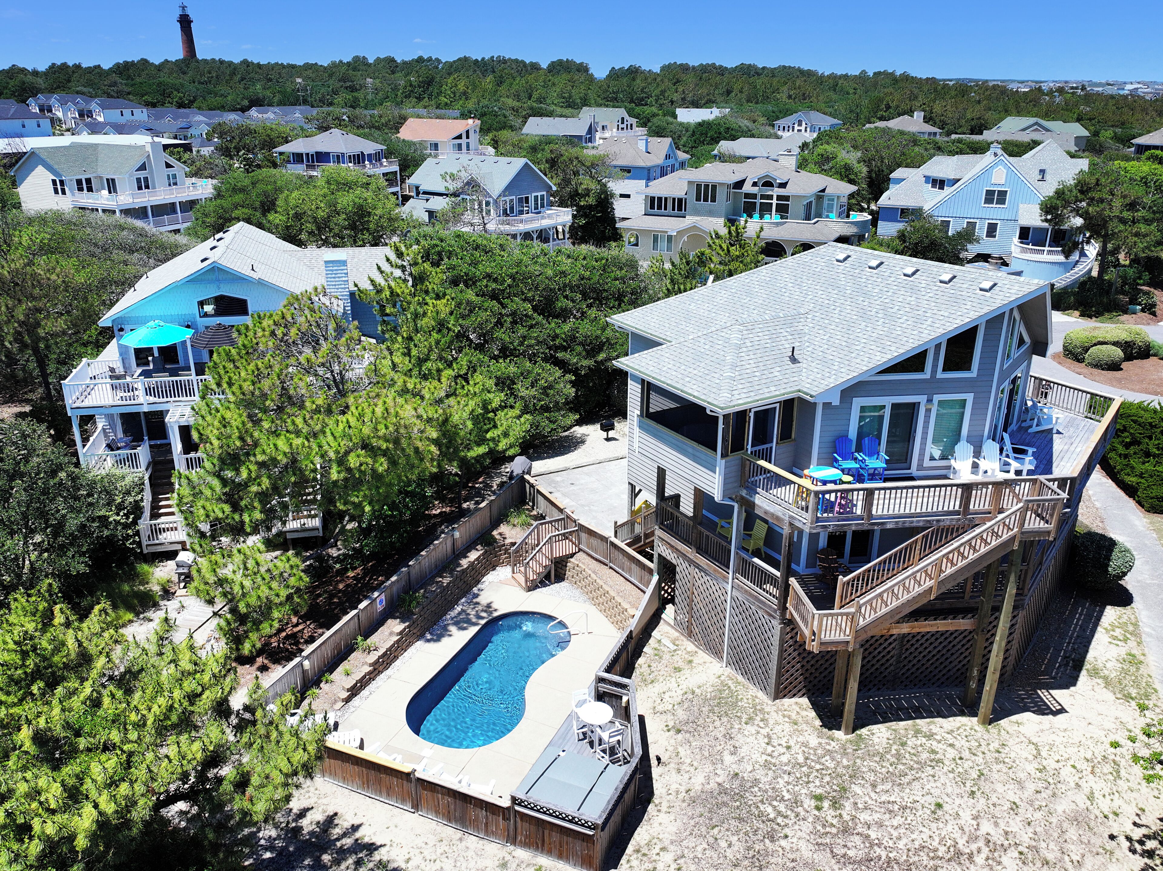 A large house with multiple decks, a swimming pool, and a lighthouse in the background.