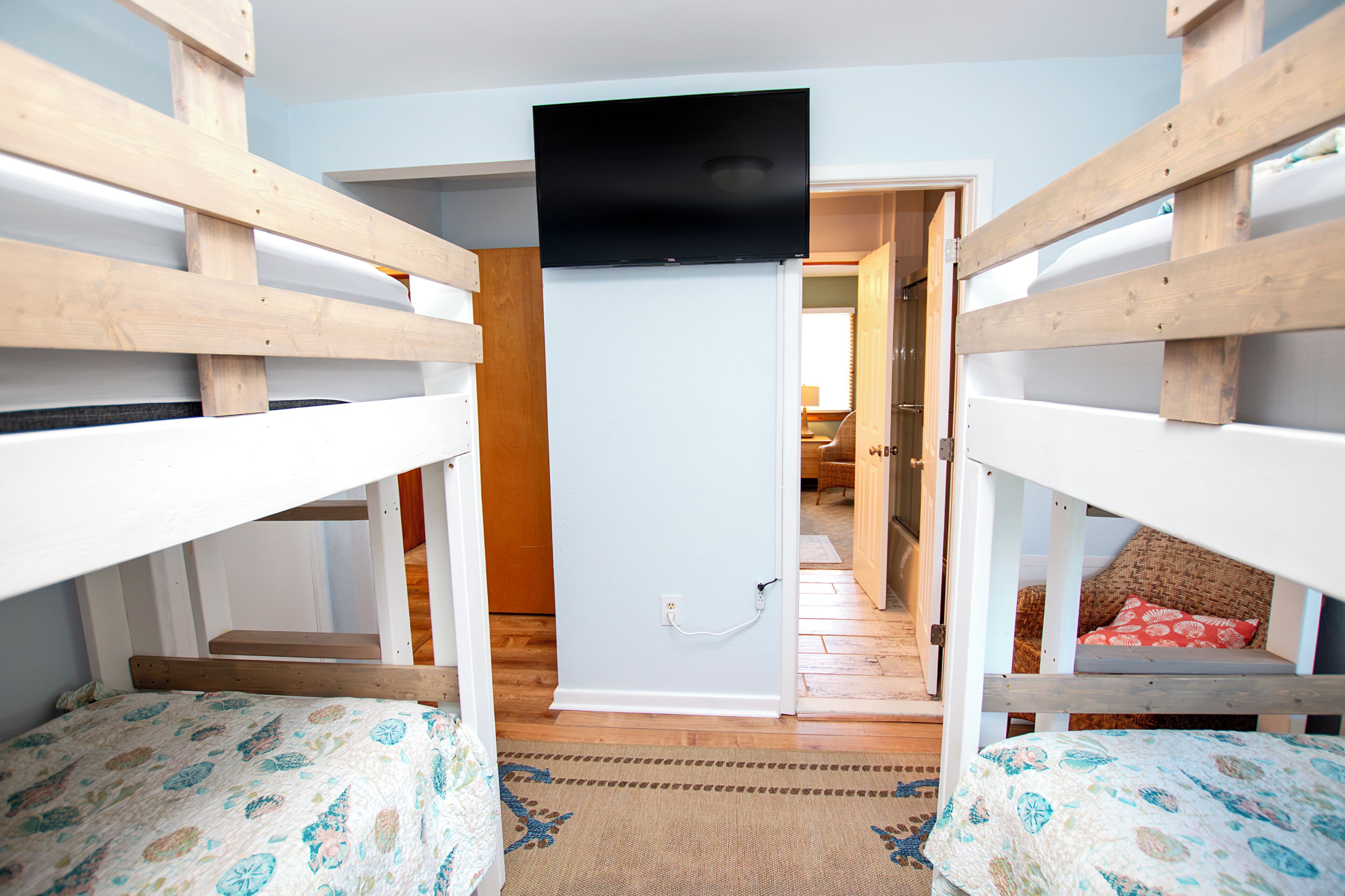 Habitación con literas, televisor sobre la puerta, piso de madera y una alfombra estampada.