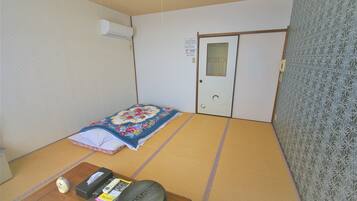 A traditional Japanese room with tatami flooring, a futon bed, a wooden desk with a telephone, and a patterned wall.