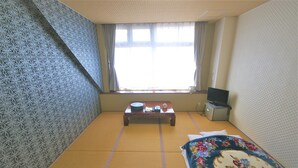 A room with tatami flooring, a futon bed, a small table with a bowl and a book, a television, and a window with curtains.