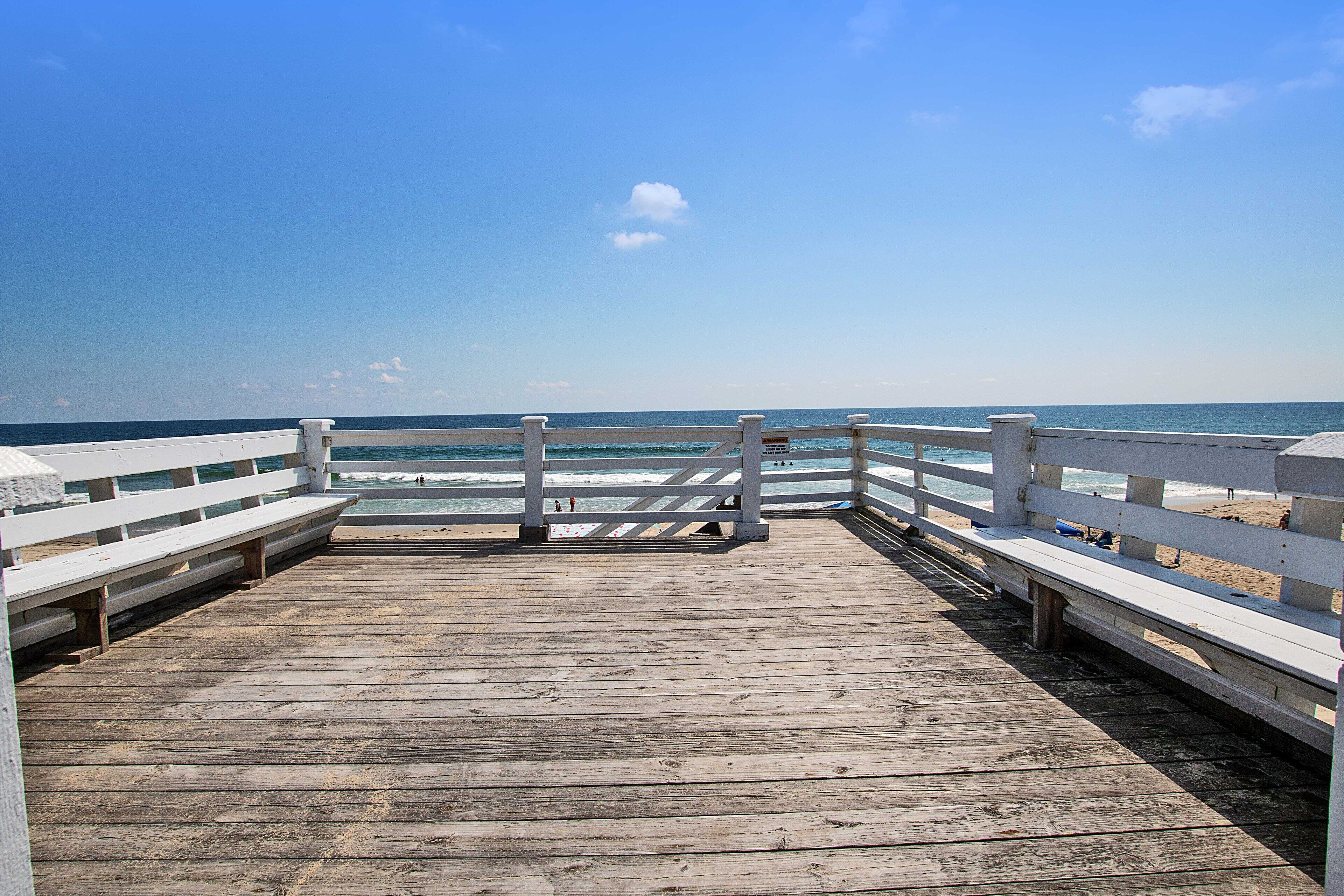 A wooden pier leading to a beach with a clear sky.