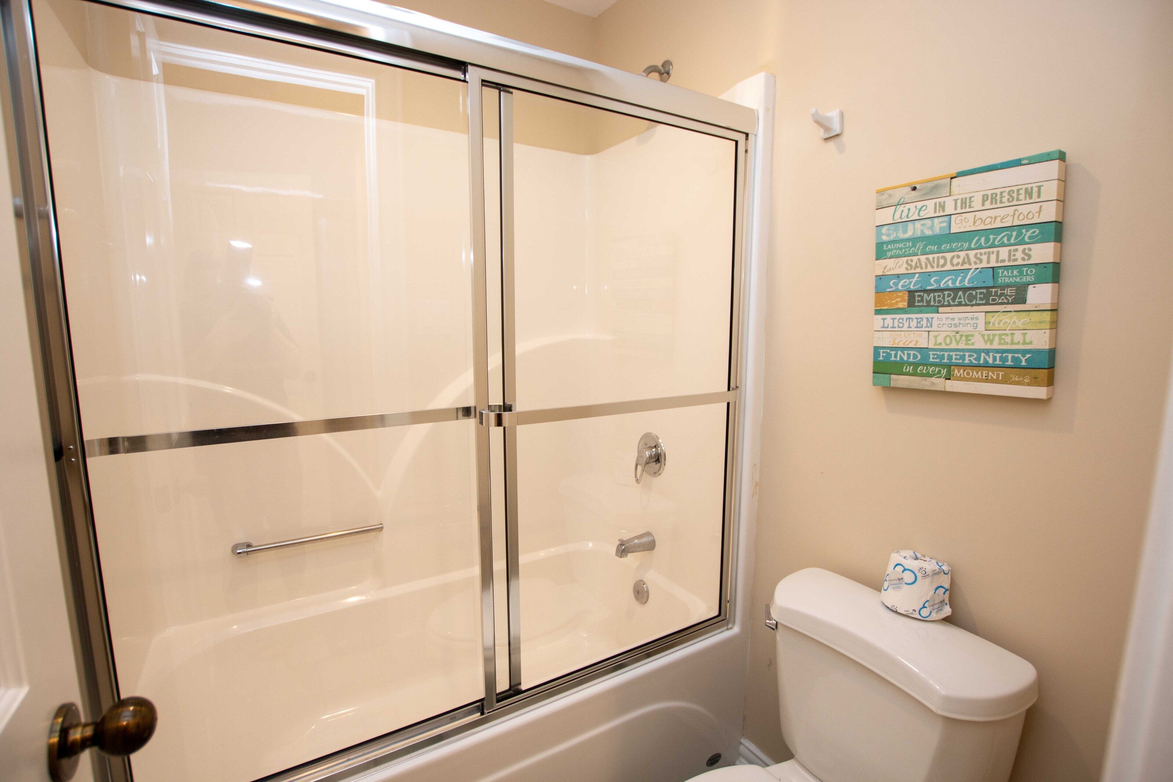 Une salle de bain dotée d’une douche à parois de verre, de toilettes et d’un panneau mural affichant des phrases motivantes.