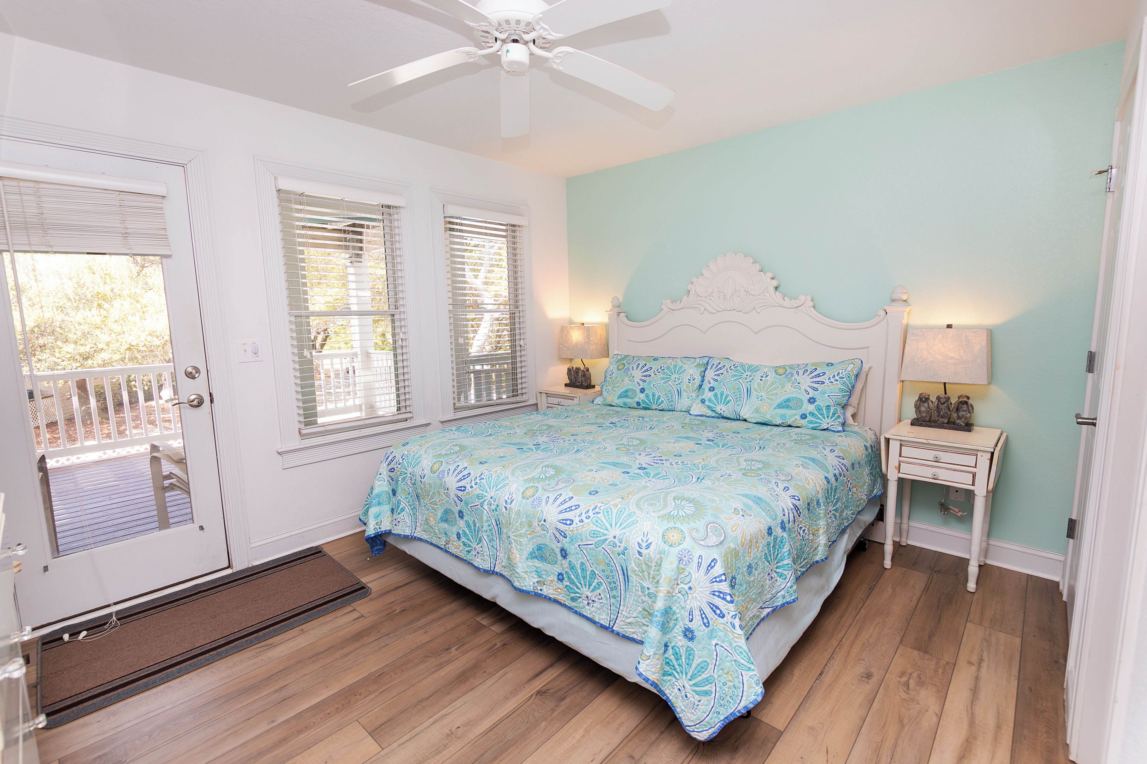 A bedroom with a bed, a nightstand, a ceiling fan, and a door with blinds.