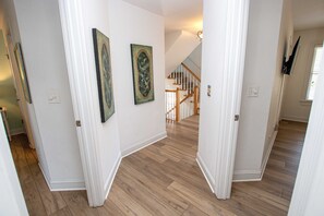 A hallway with wooden flooring, white walls, and a staircase in the background. - Soundfront, Dog Friendly, Private Pool, Rec Room, 549, Sunrise Sunset (Corolla)