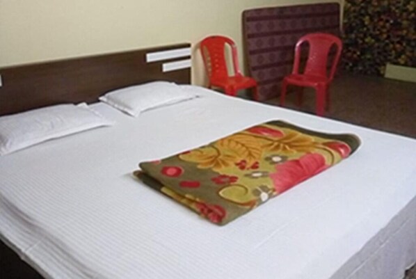 Una cama con sábanas blancas, una manta de estampado floral y dos sillas de plástico rojo.