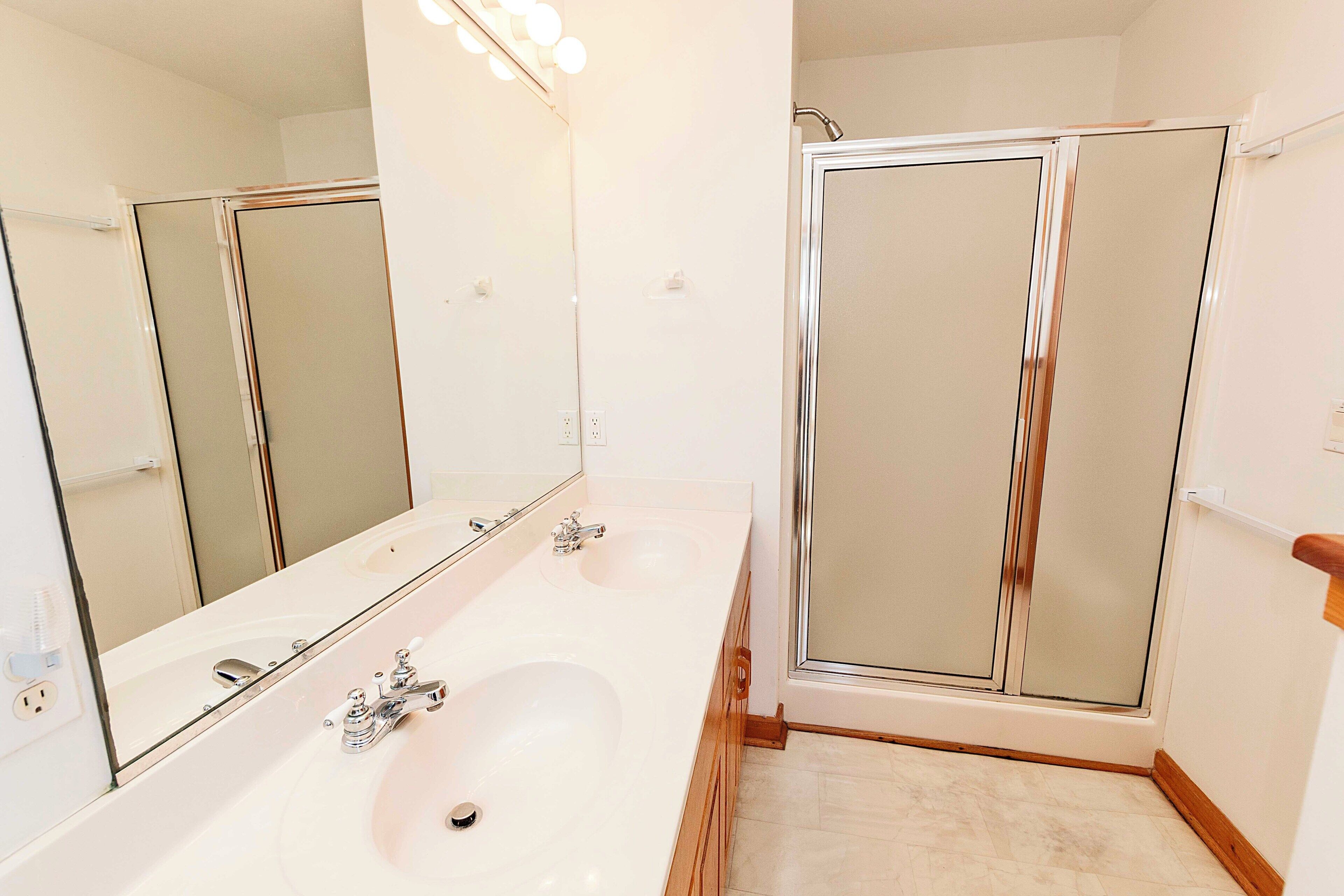 A bathroom with a double sink, a large mirror, and a glass-enclosed shower.